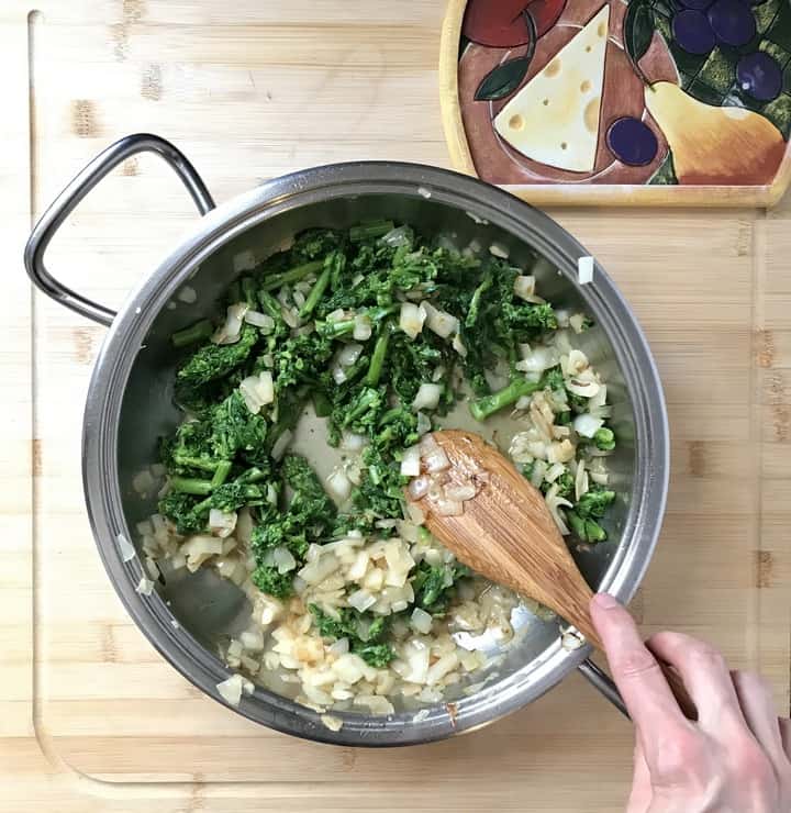 Parboiled Broccoli rabe added to sauteed onions and garlic in a pan.