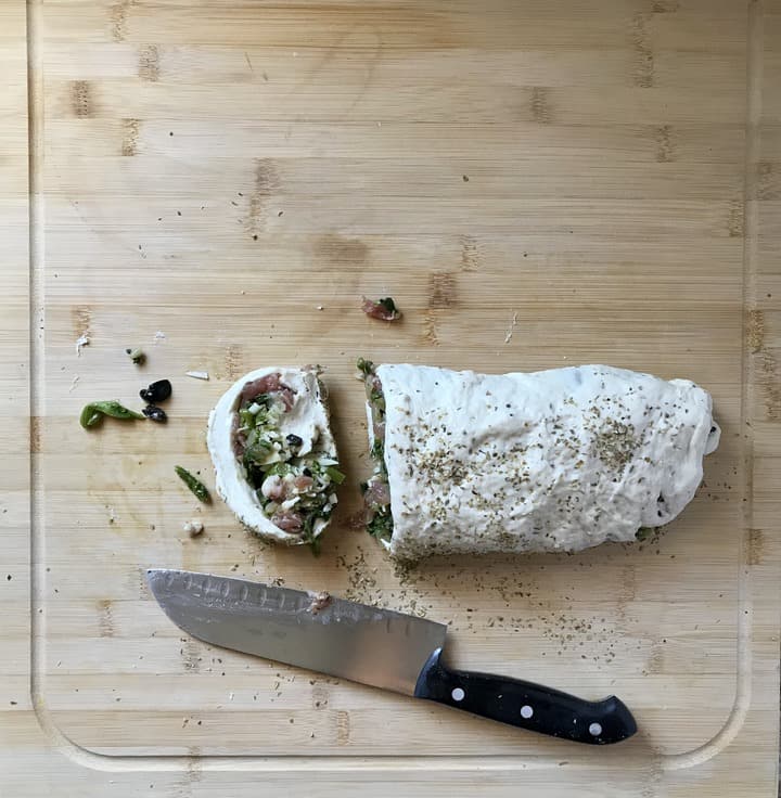 A pizza rolls slice on a wooden board next to a knife.