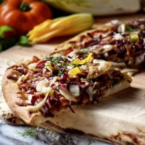 A piece of pizza topped with endive, radicchio and fennel, on a wooden board.