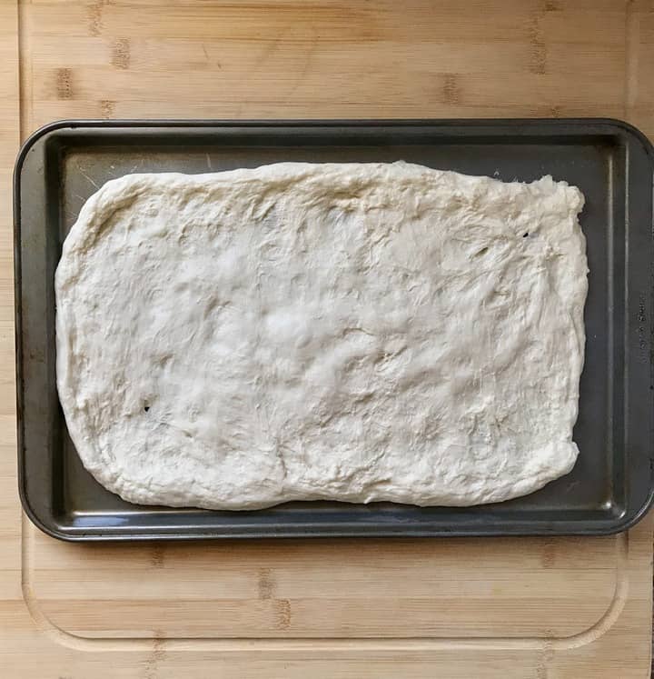 Pizza dough is stretched out on a baking sheet pan.