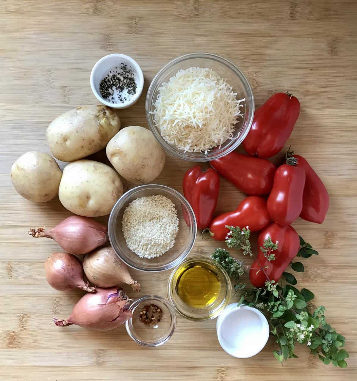 Ingredients like potatoes and tomatoes on a wooden board to make a vegetable bake recipe.