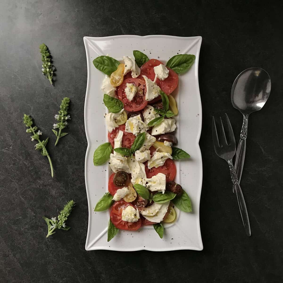 A mozzarella, basil and tomato salad aka caprese in white serving dish.