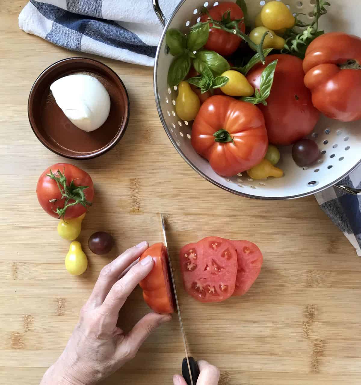 Heirloom tomatoes being sliced to make a caprese salad.