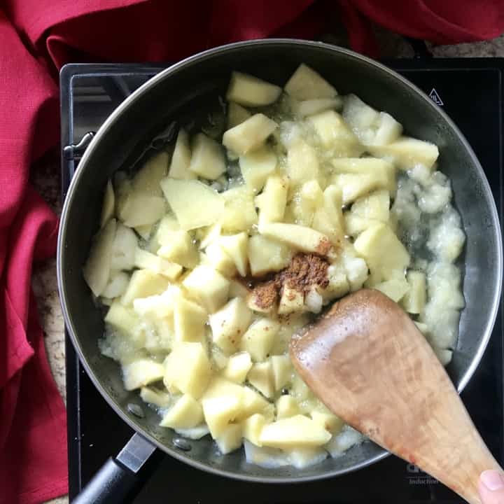 Ground cinnamon sprinkled on partially cooked apples in a sauce pan.