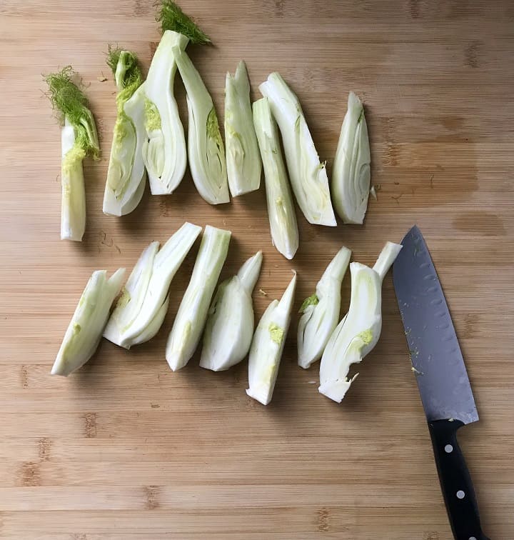 Fennel bulbs sliced in quarters, on a wooden board.