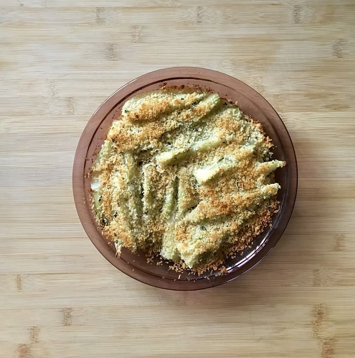 A round casserole dish of cooked fennel on a wooden board.