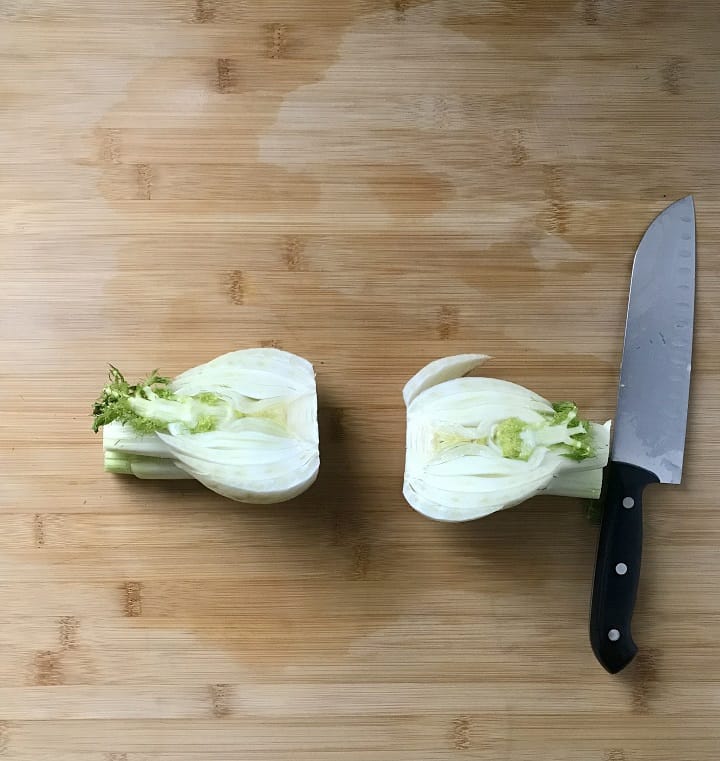 A fennel bulb, cut in half, on a wooden board.