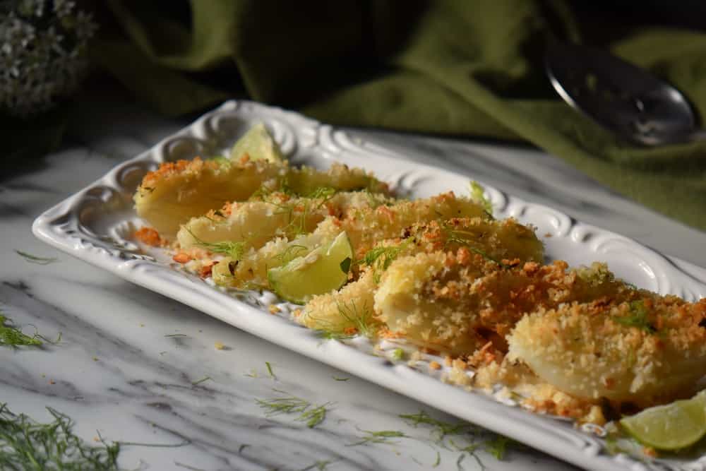 Baked fennel garnished with bread crumbs and fennel fronds in a white dish.