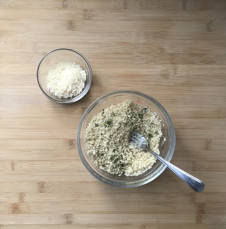 A large bowl with Panko bread crumbs and herbs next to a bowl of grated cheese.