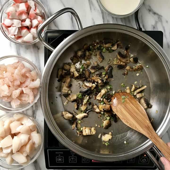 Small bowls of shrimp, scallops and crab about to be sauteed with mushrooms that ate already in a large pan.