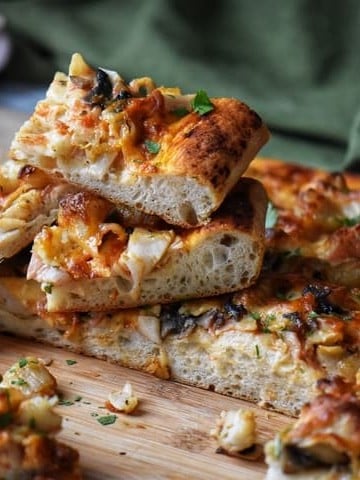 Slices of seafood pizza garnished with fresh parsley on a wooden board.