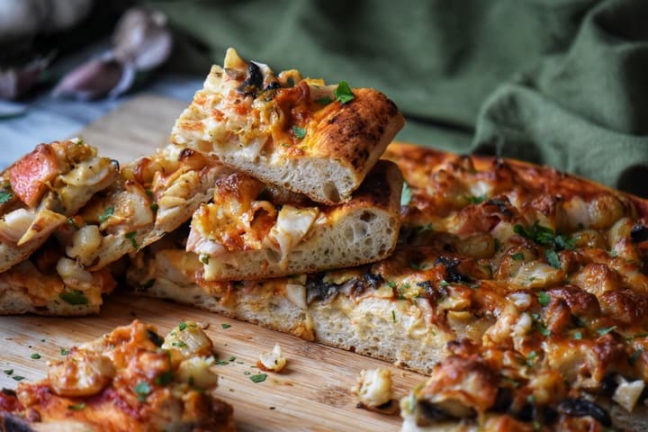 Slices of seafood pizza garnished with fresh parsley on a wooden board.