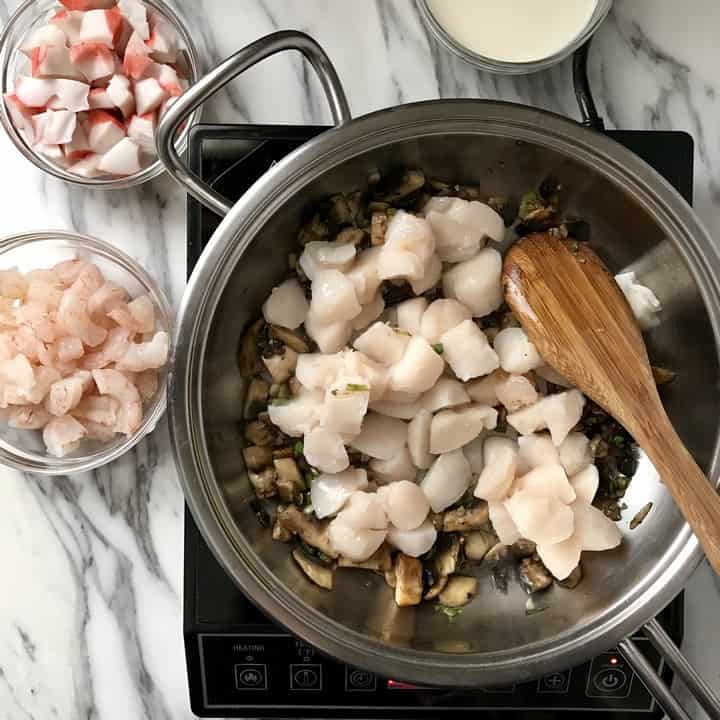 Scallops in the process of being sauteed in a large pan.