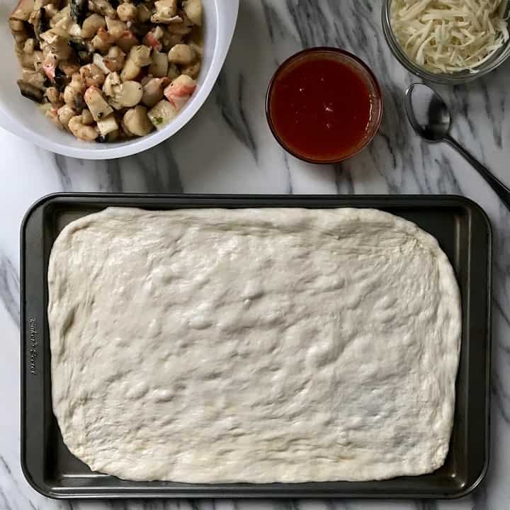 Stretched out pizza dough next to a bowl of seafood mixture, pizza sauce and freshly grated mozzarella.