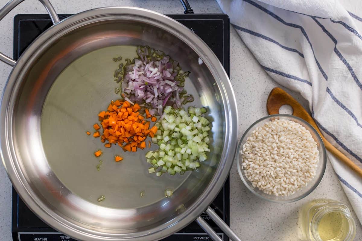 Chopped carrots, onion and celery are being sauteed in a large saucepan.