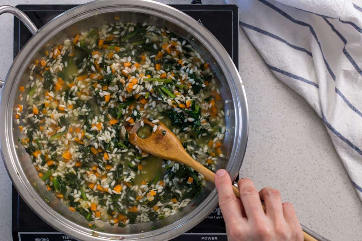 A risotto spoon is used to stir the spinach risotto.