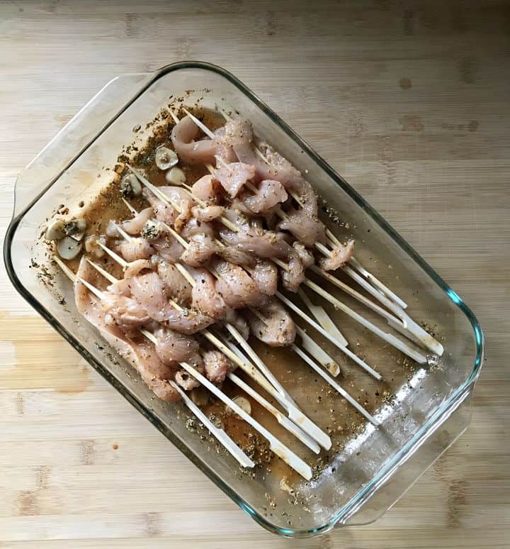 Chicken skewers are being marinated in a large shallow dish.