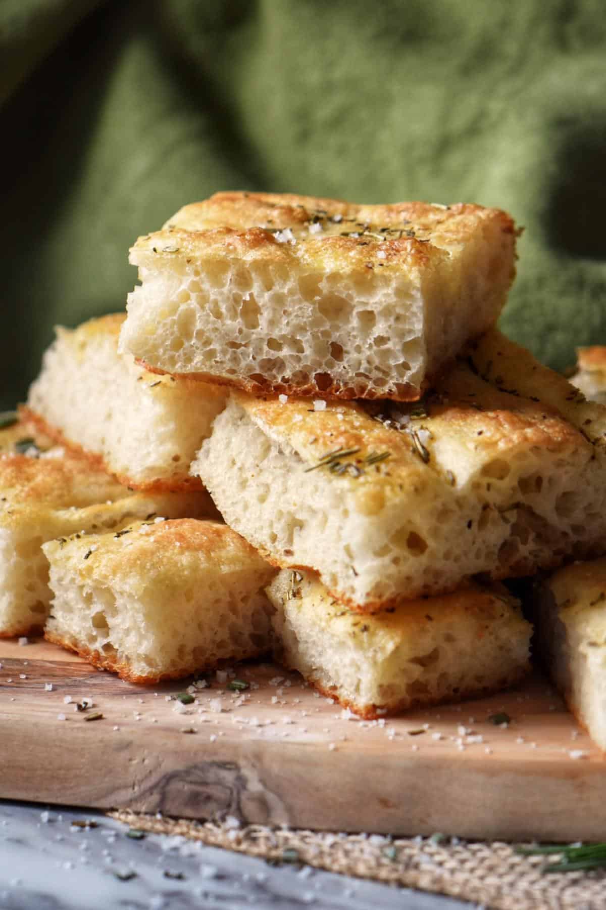 Slices of focaccia bread piled high on a wooden board.