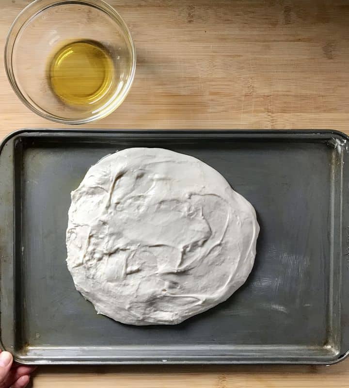 The wet dough of focaccia on a rimmed baking sheet.