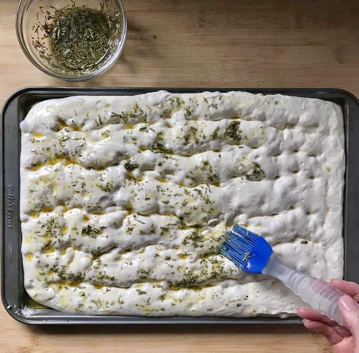 A rosemary herb topping is spread over the focaccia bread.