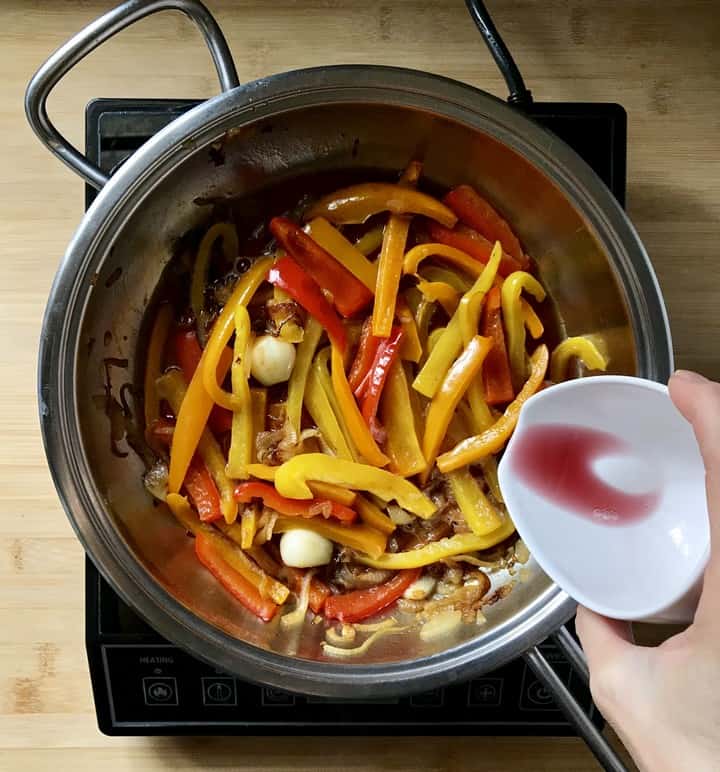 Wine is being added to the sauteed peppers in a saucepan.