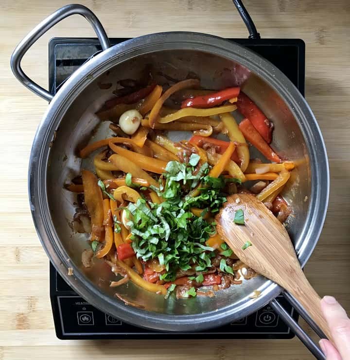 Chopped parsley and basil is added to the pan of bell peppers.