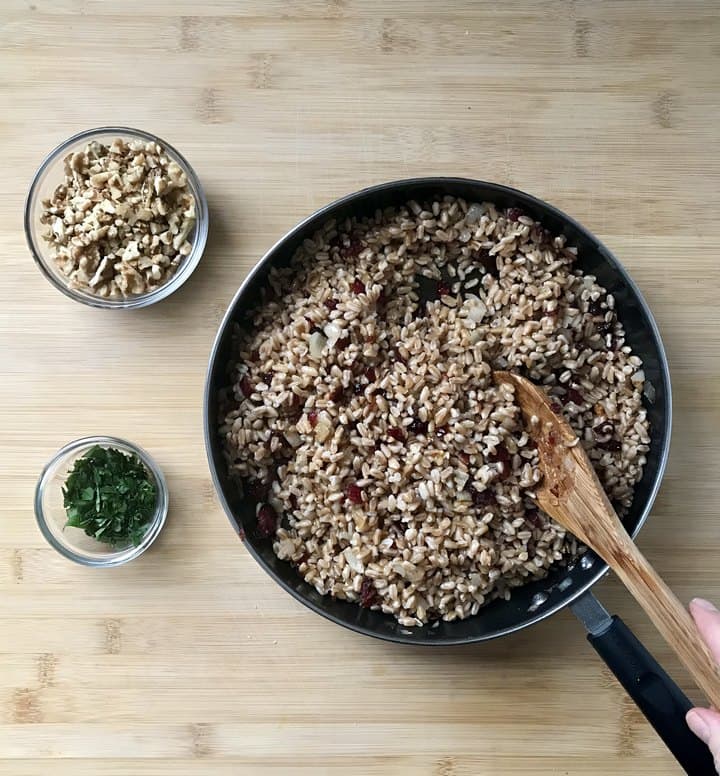 Chopped walnuts and parsley in bowls, next to a pan of warm farro.