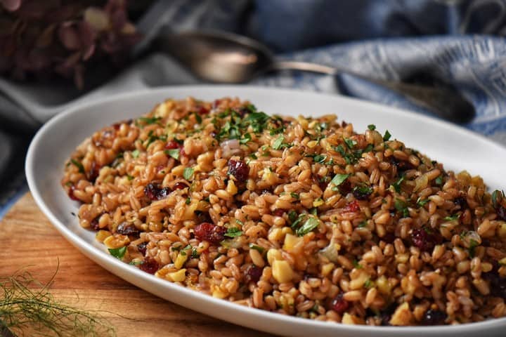 A white serving platter of Italian farro salad on a wooden table.