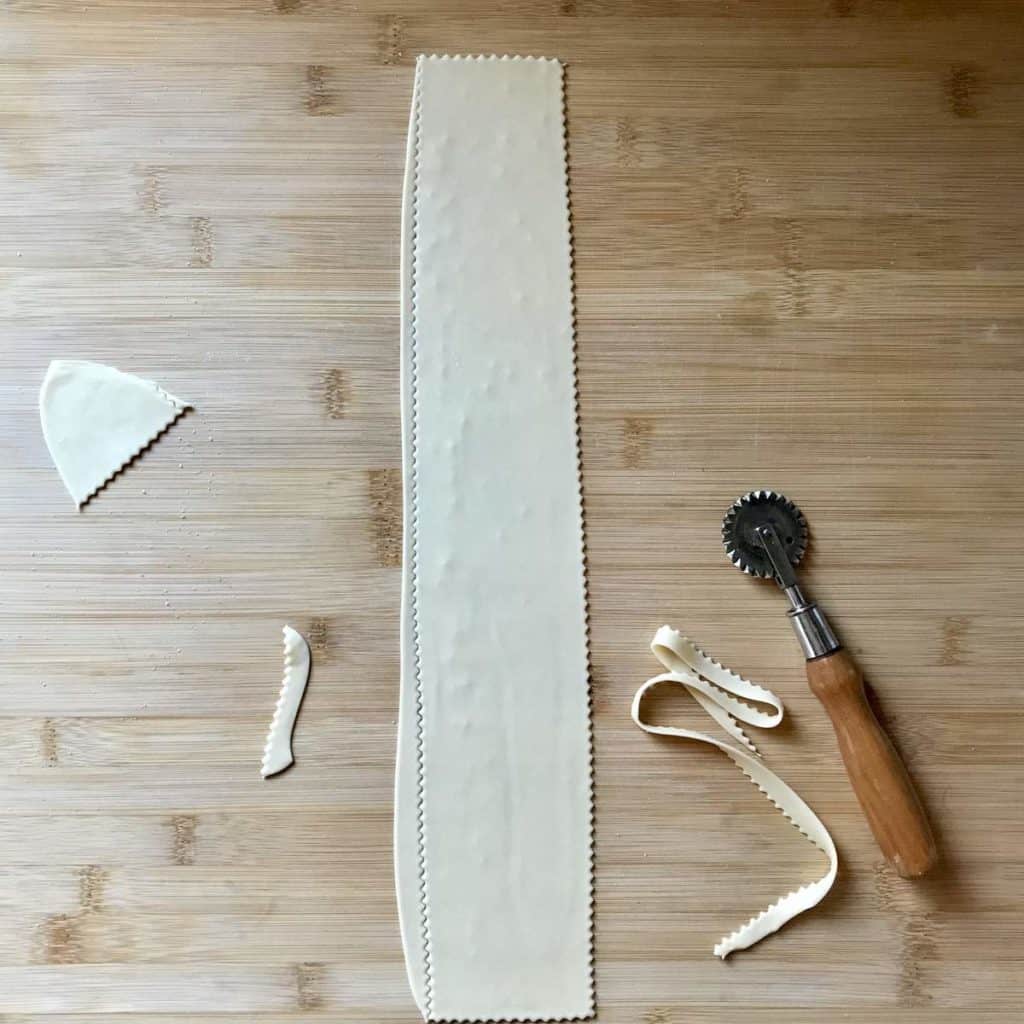 A pastry wheel is used to cut a piece of dough on a wooden board.