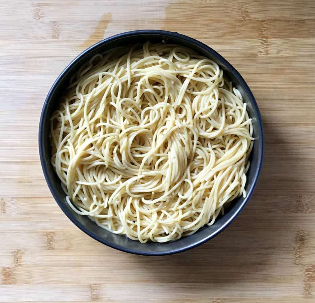 A round pan filled with a spaghetti mixture on a wooden board.