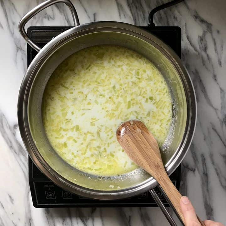 The beginnings of a bechamel sauce is being stirred by a wooden spoon.