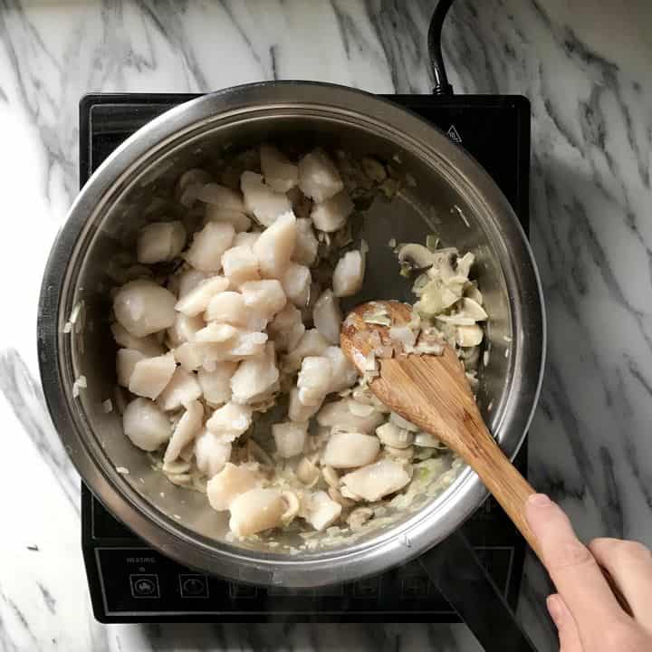 Scallops being sauteed in a saucepan to make Coquilles St-Jacques.