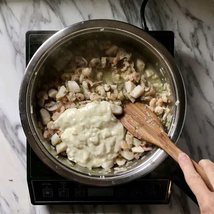 The bechamel sauce is added to the seafood mixture.