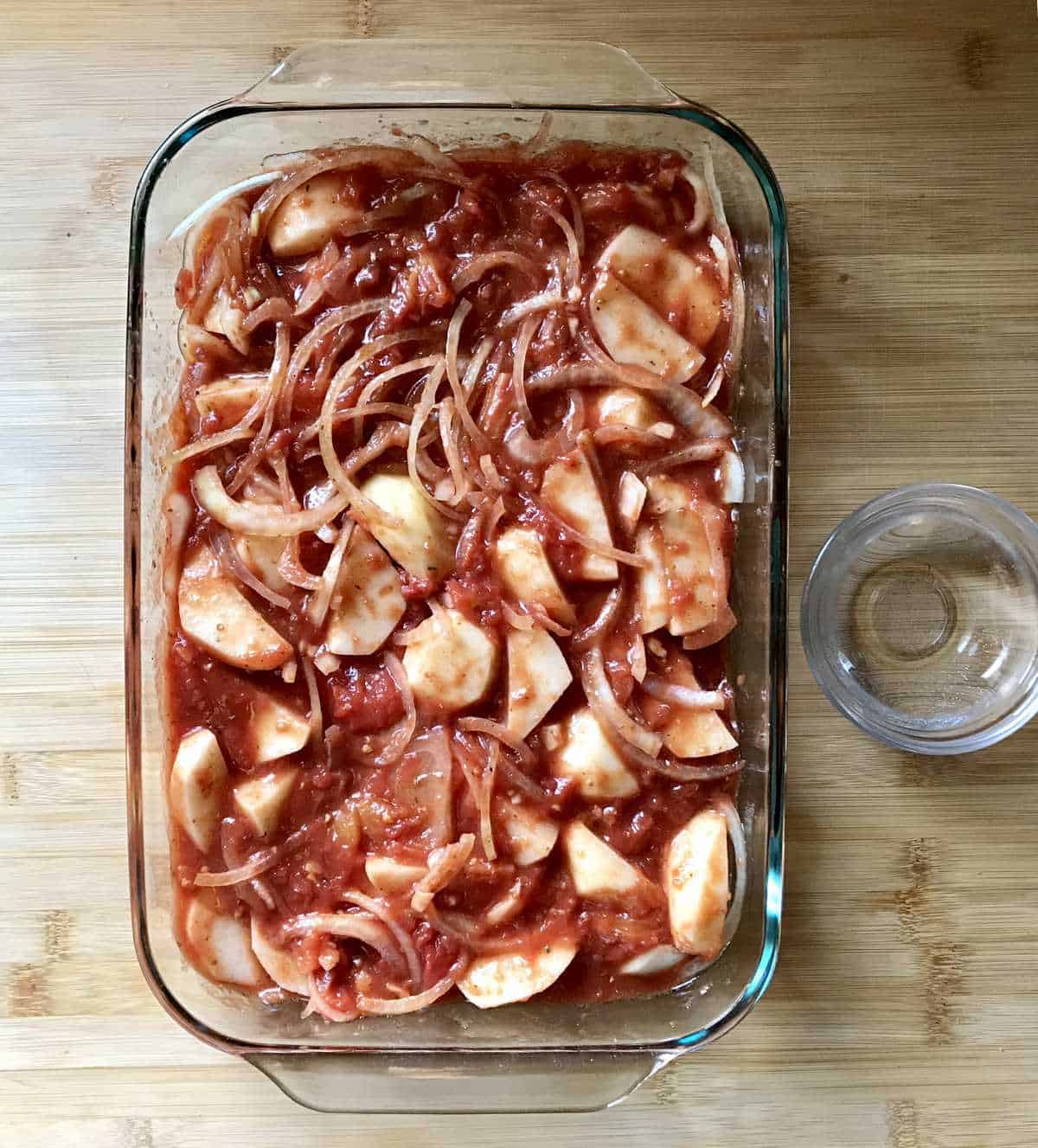 Onions and tomatoes are combine with potato wedges in a large rectangular baking dish.