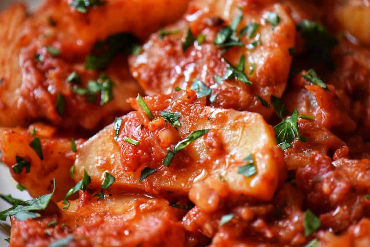 Potato wedges in a tomato sauce, garnished with fresh chopped parsley.