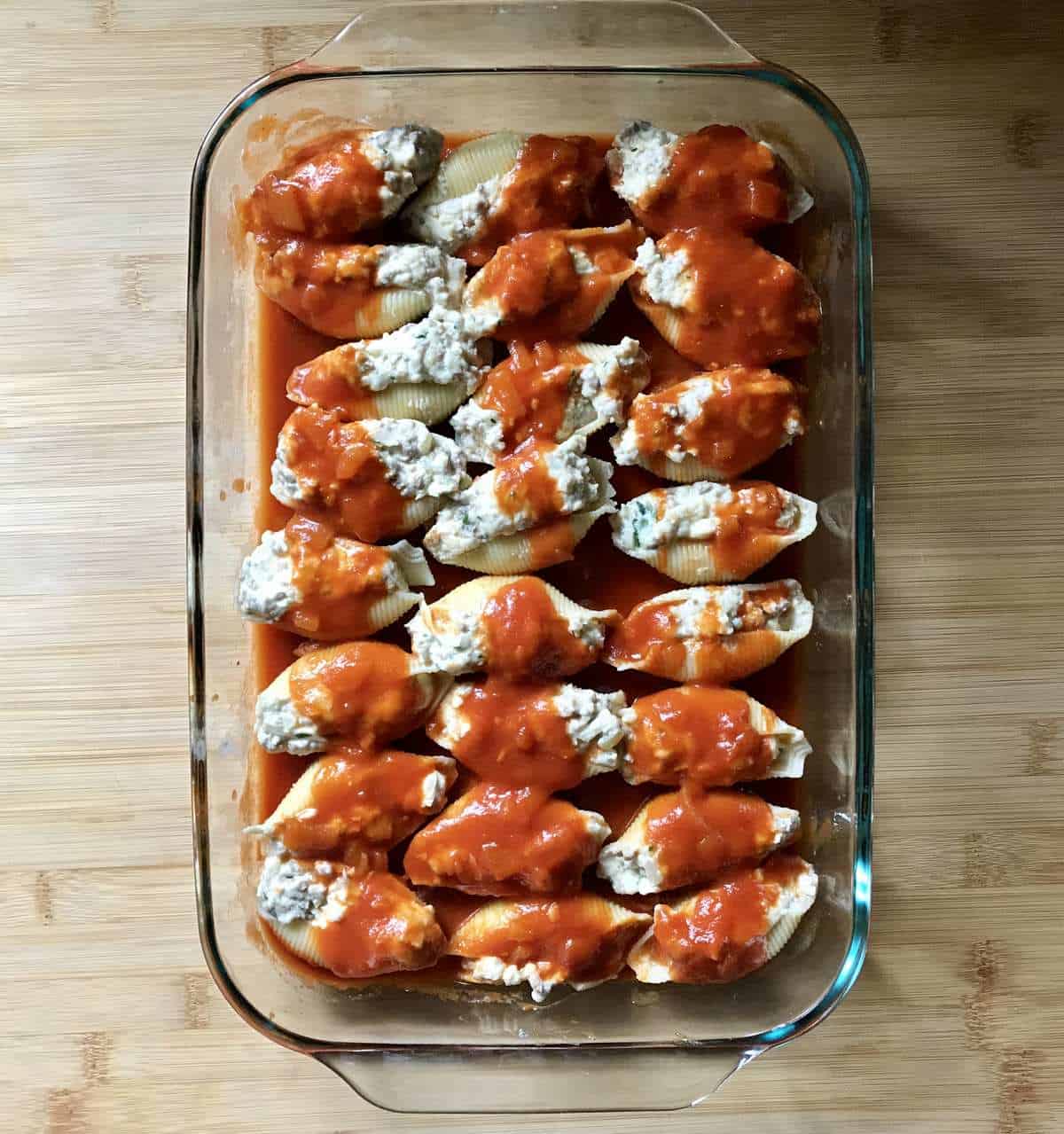 Pasta shells in a larger caserole dish topped with tomato sauce.