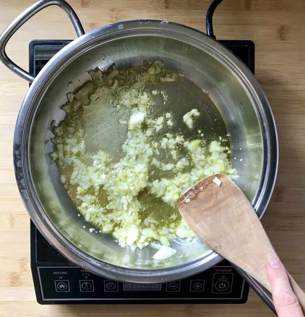 Chopped garlic and minced onions are sauteed in a large frying pan.