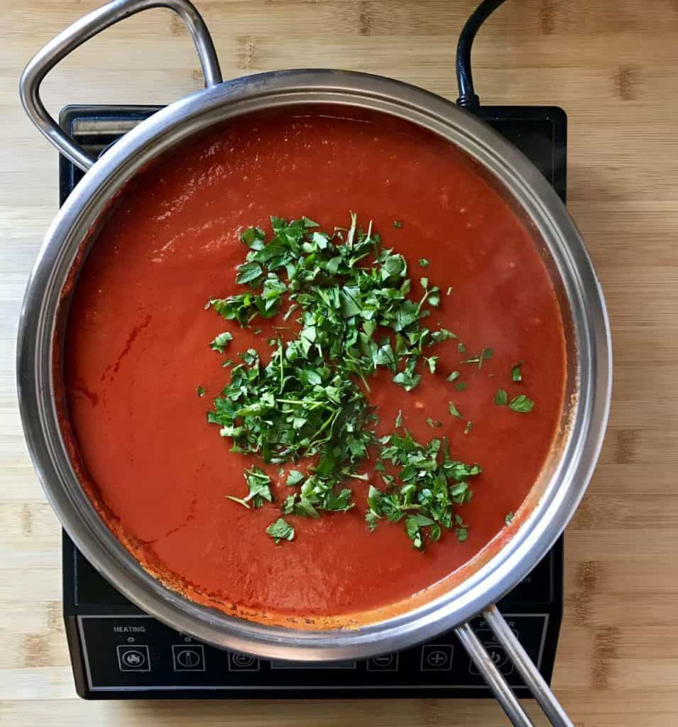 Chopped parsley added to a saucepan of tomato sauce.