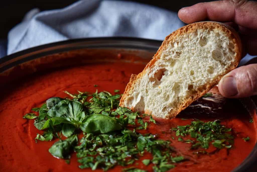 A piece of Italian bread being dunked in tomato sauce.