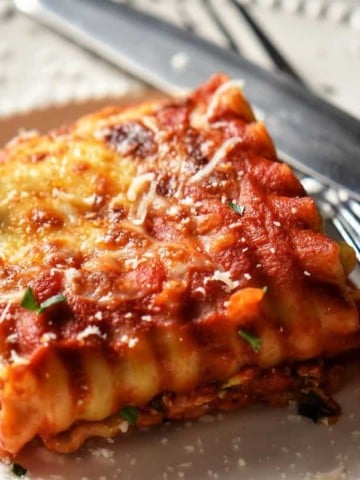 The cheesy top of a lasagna roll up on a white ceramic dish.