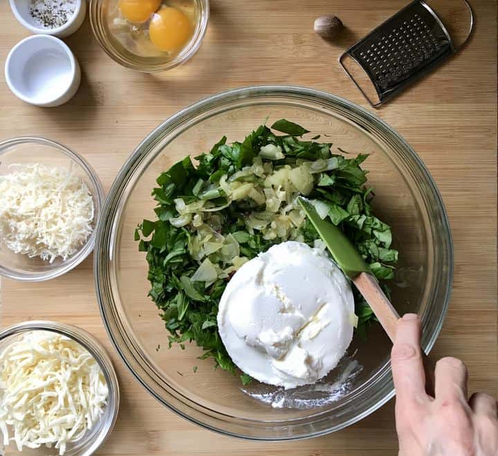 A spinach ricotta mixture is combined in a large mixing bowl.