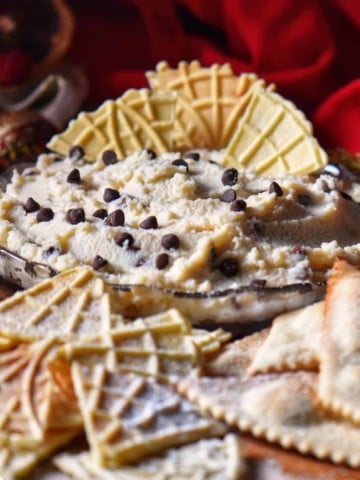 Cannoli dip in a serving dish surrounded by pizzelle.