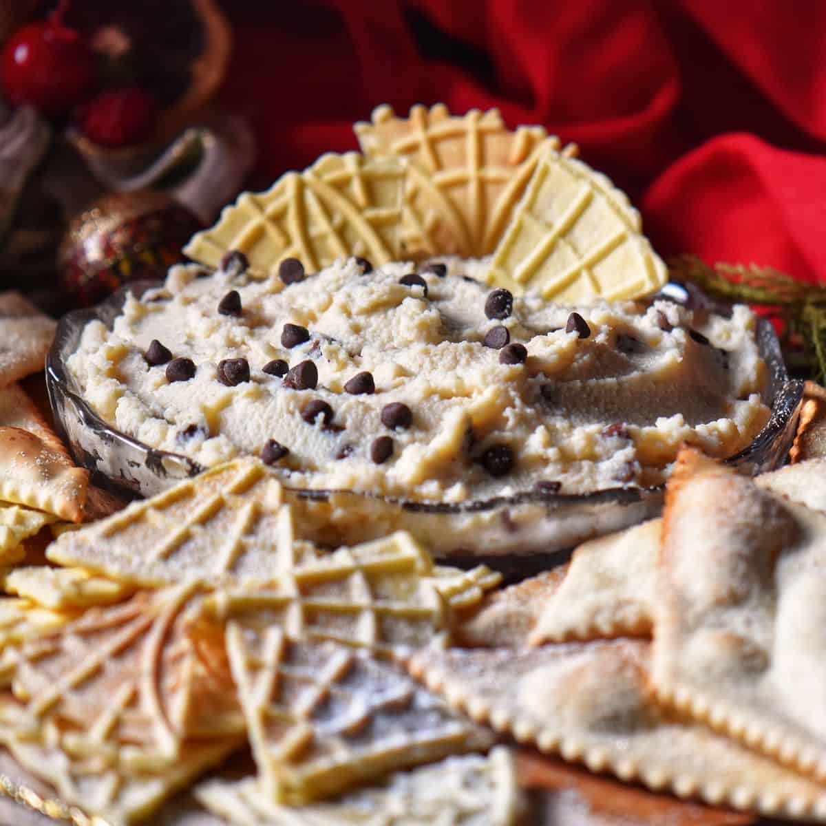 Cannoli dip in a serving dish surrounded by pizzelle.