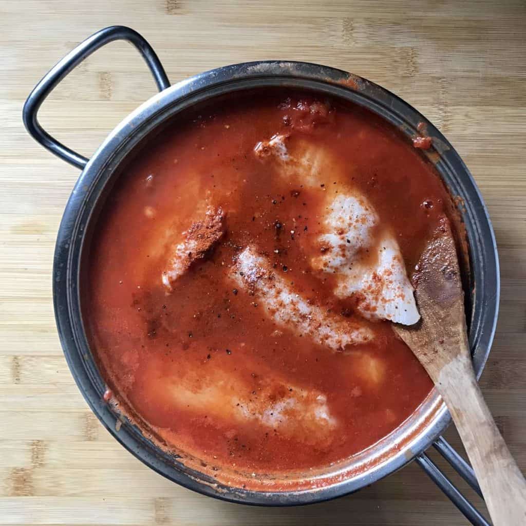 Cod fillets are added to the tomato sauce.