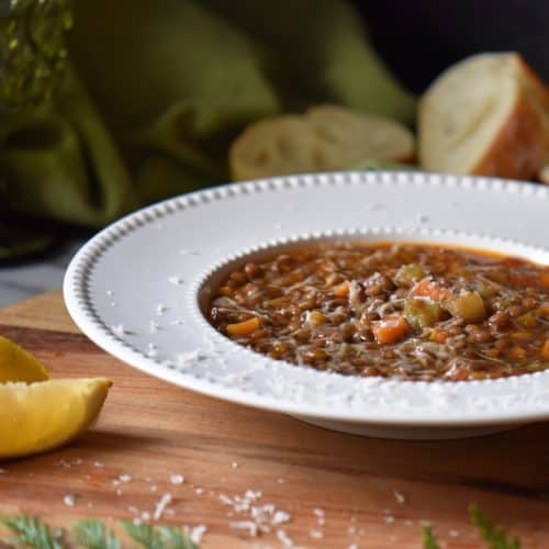 Italian Lentil soup in a white bowl next to a lemon wedge.