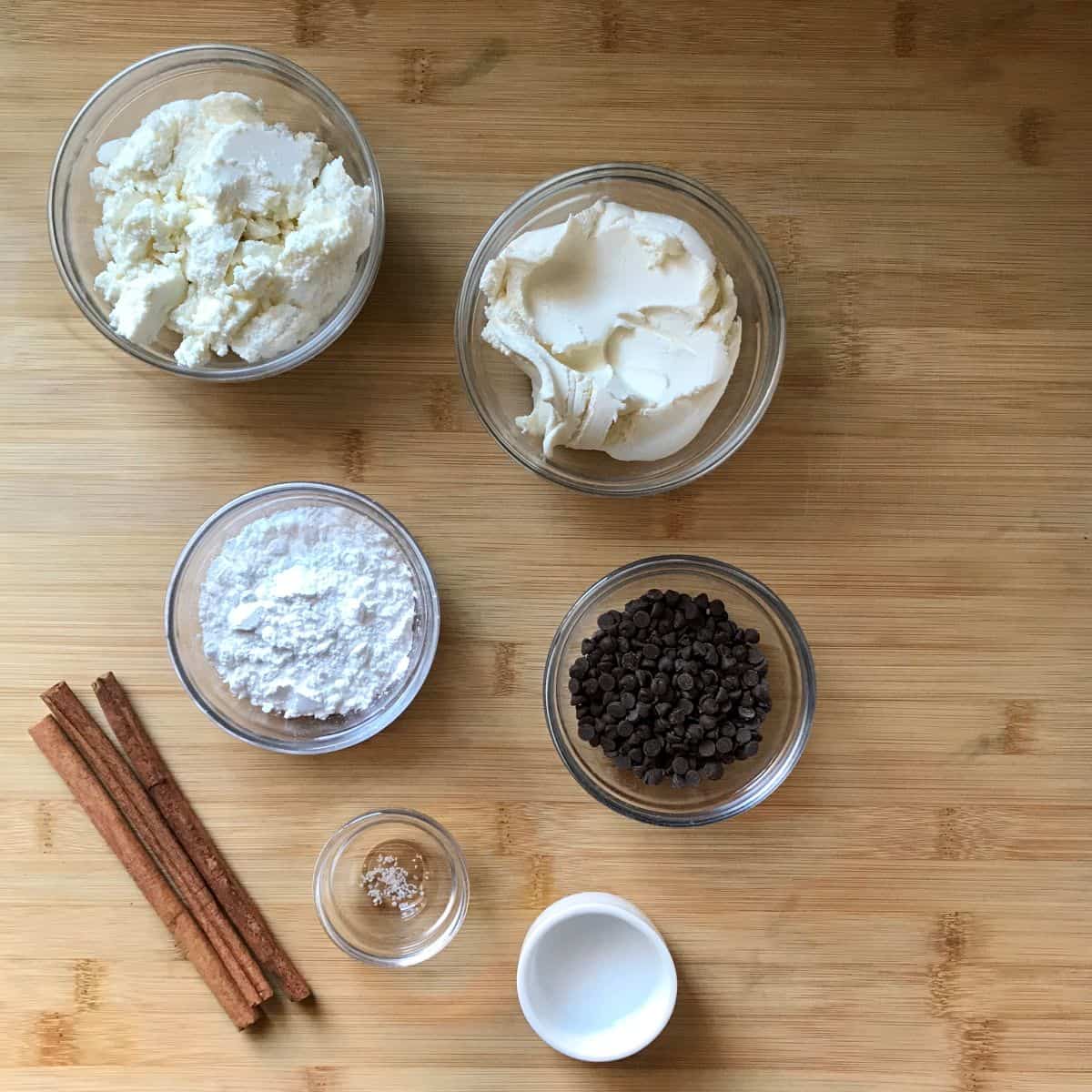 Ingredients to make a cannoli dip recipe on a wooden board.