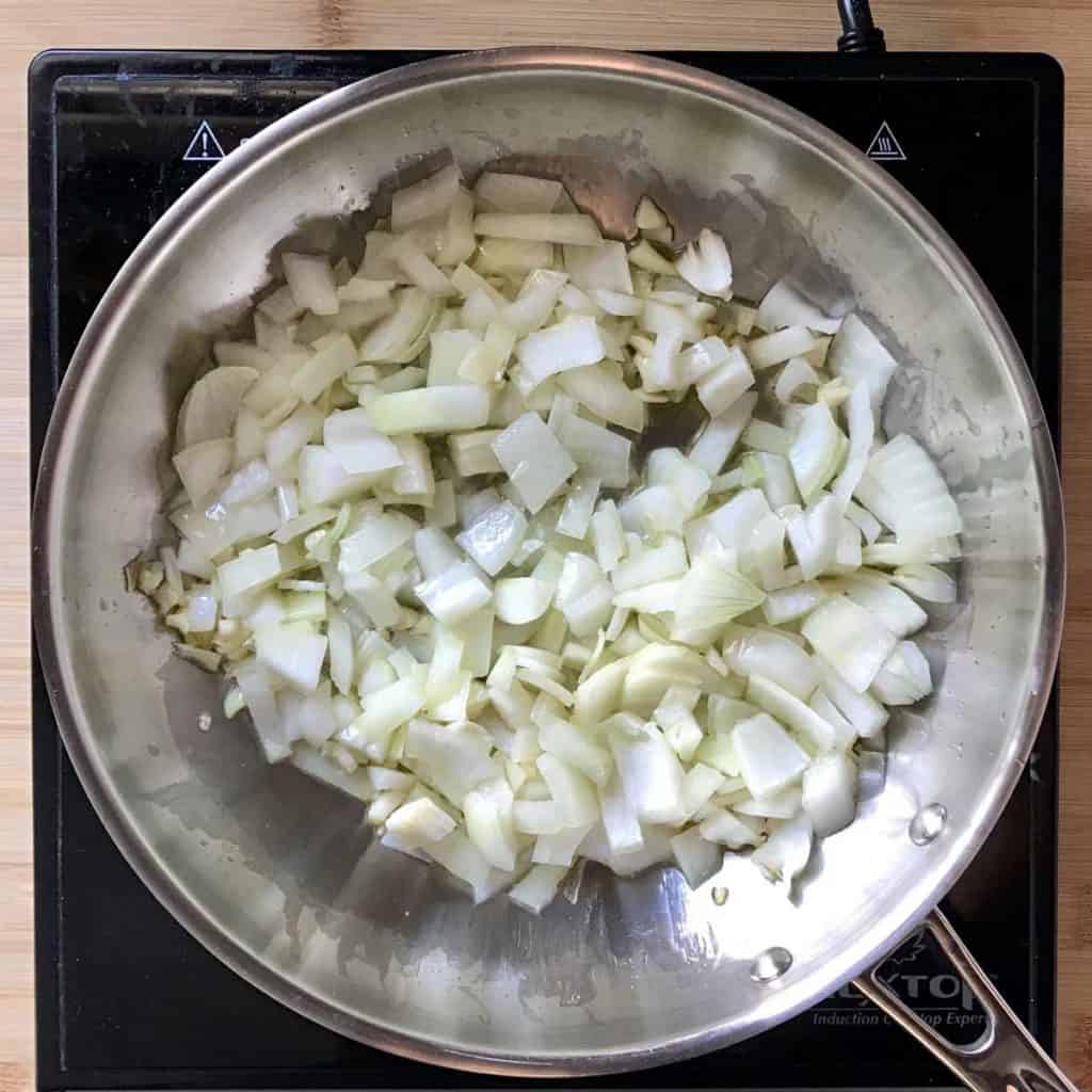 Chopped garlic and minced onions are sauteed in a large frying pan.
