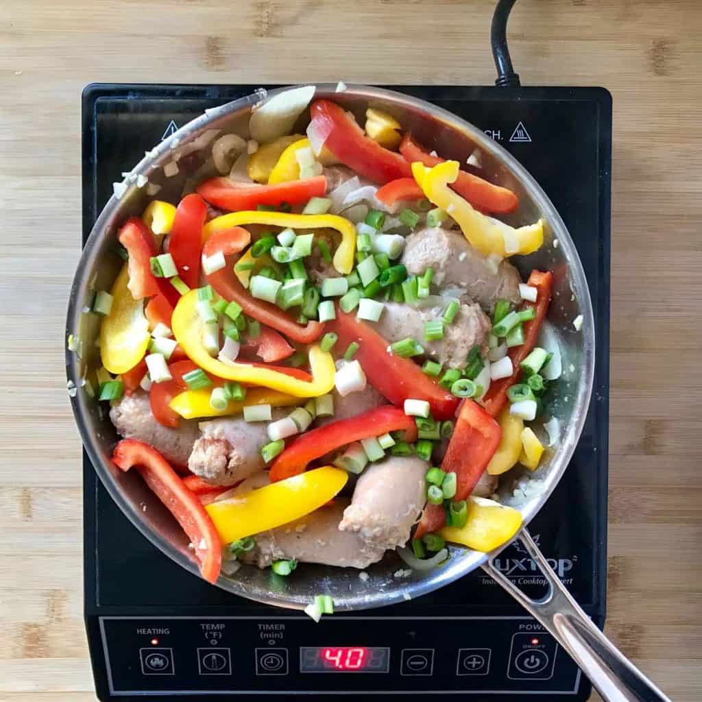 Red and yellow peppers added to the skillet with the sausages and the onions.