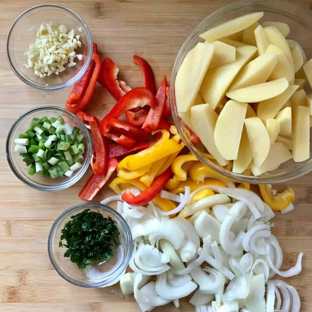 Chopped potatoes, peppers, onions and garlic on a wooden board.