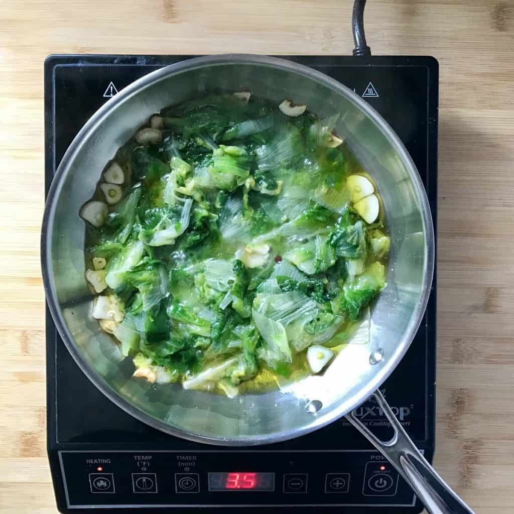 Parboiled escarole added to a frying pan.